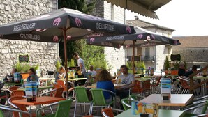 Un café en plein air avec des tables et des chaises, des parasols et un mur de pierre en arrière-plan.