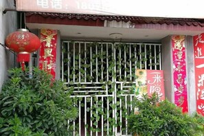 Fachada de edifício com portão de metal, faixas vermelhas com caracteres chineses e um lança-luz vermelho.