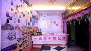 Un comptoir d’accueil aux couleurs rose et blanc, entouré d’un mur décoré de photos et d’une carte. Deux tabourets de bar noirs sont placés devant le comptoir.