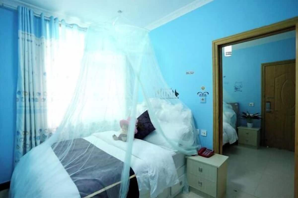 Un dormitorio con una cama bajo una mosquitera, una mesita de noche y un buró.