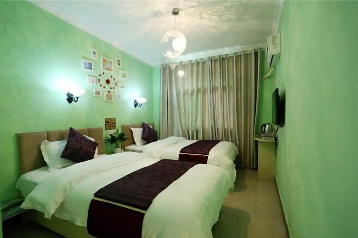 Habitación de hotel con dos camas, ventilador de techo, un reloj de pared y ventana con cortinas.