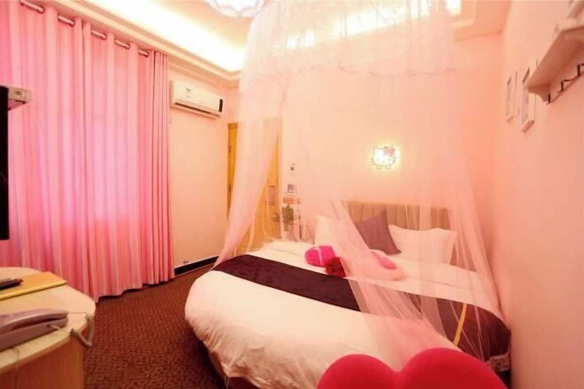 Una habitación de hotel con cama, mesita de noche, silla, cortina y ventana.