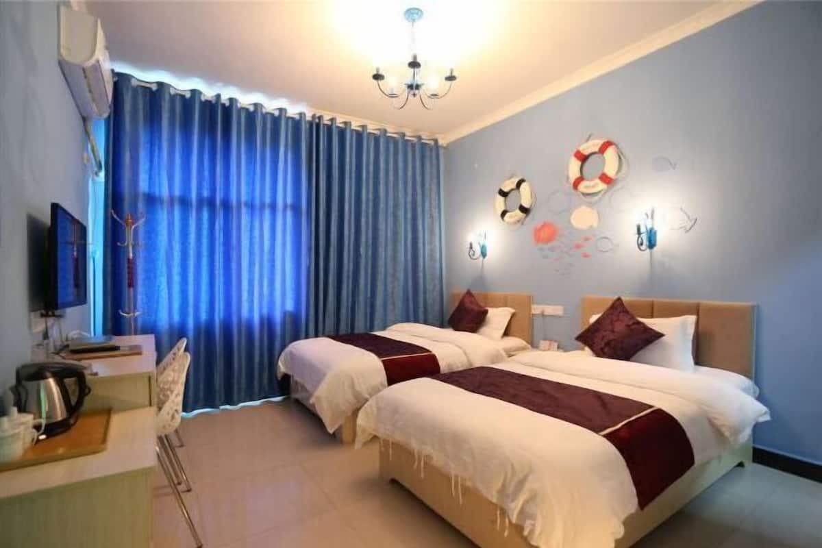 Habitación de hotel con dos camas, un escritorio con hervidor, una silla y un televisor.
