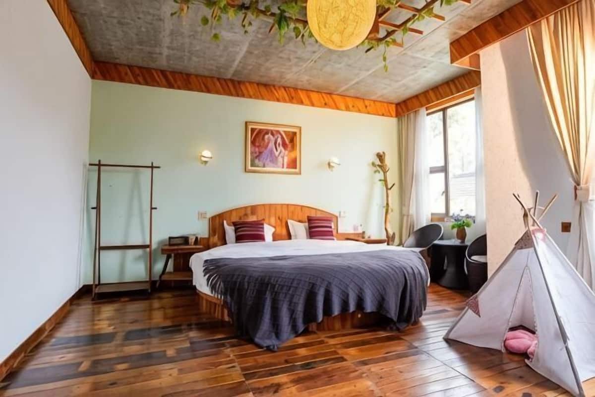 Un dormitorio con cama, cabecera de madera, lámpara colgante, ventana con cortinas e indio.
