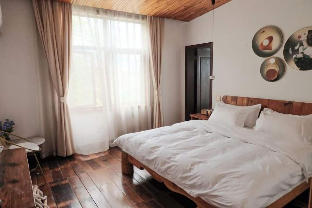 Un dormitorio con cama de madera, mesita de noche, cortinas translúcidas y decoración en la pared.