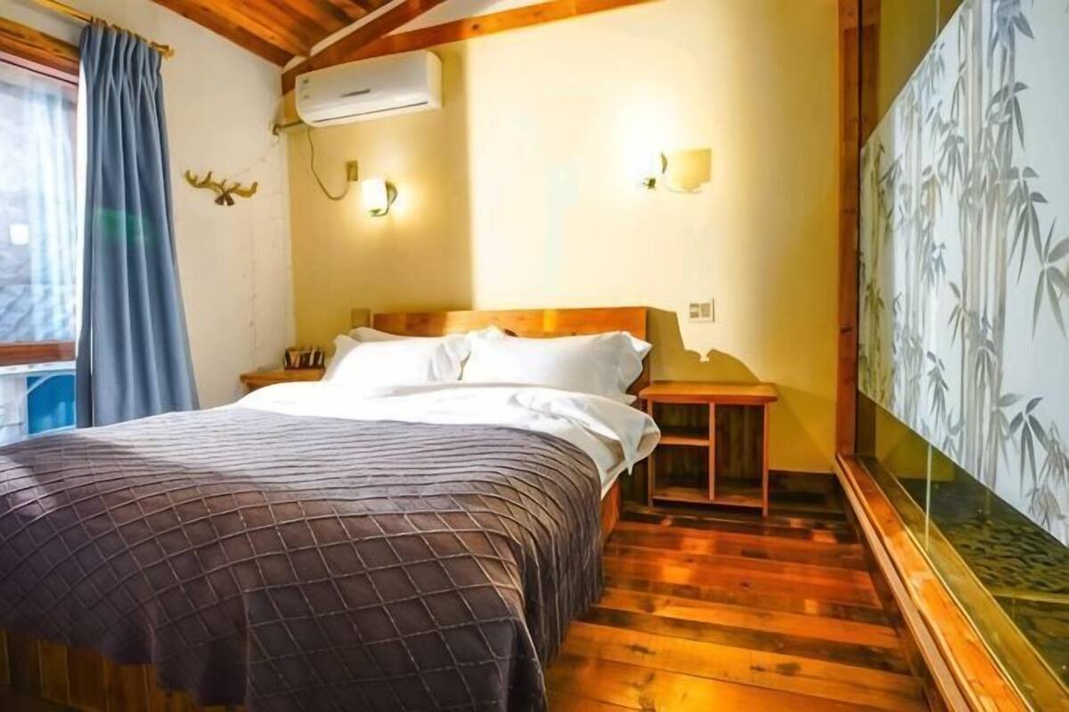 Un dormitorio con cama, suelo de madera, aire acondicionado de pared, lámparas de noche y un adorno en la pared.