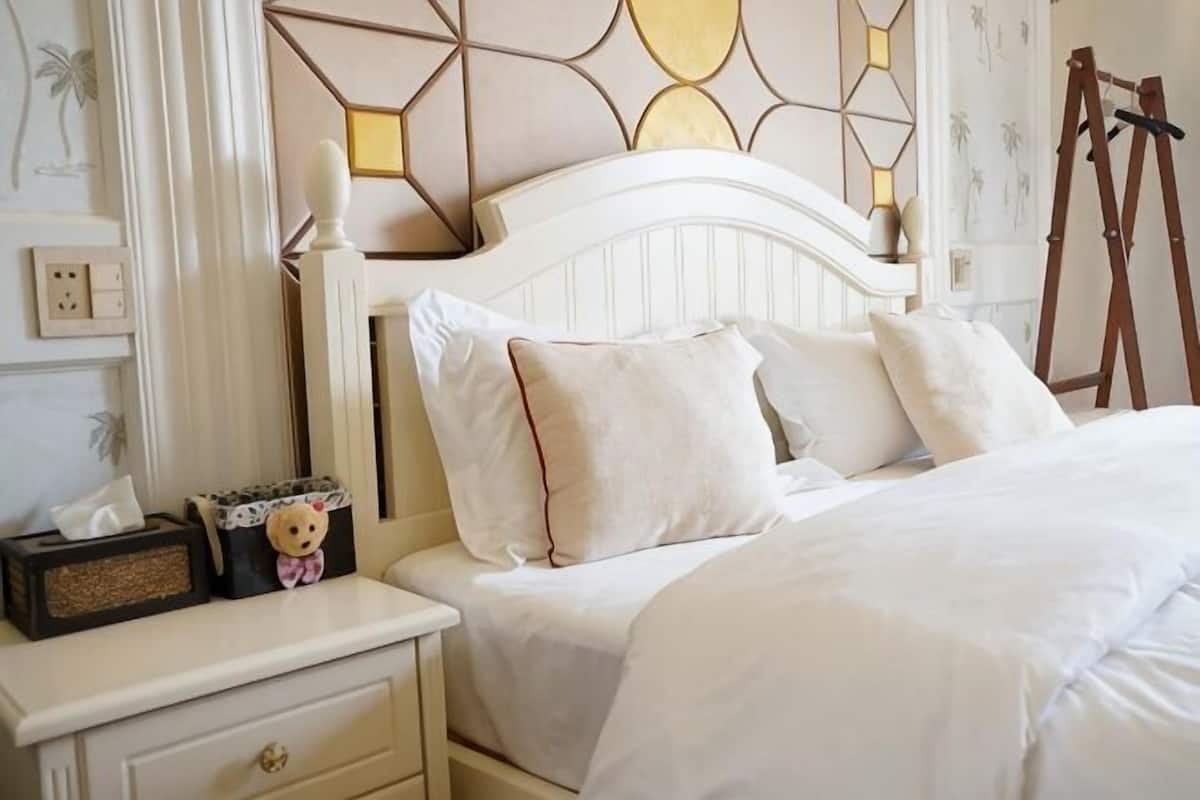 Una cama bien hecha con almohadas, una mesita de noche con lámpara y una pared con diseños geométricos.