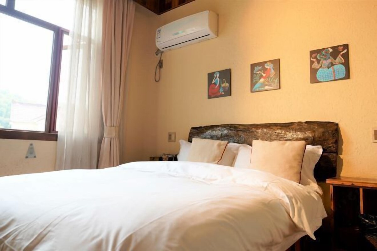 A bedroom with a large bed, an air conditioning unit, and three paintings on the wall.