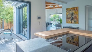 A modern kitchen with a large island, sliding glass doors leading to a patio, and a dining area visible through the glass. - La Provence et ses cigales (Ceyreste)