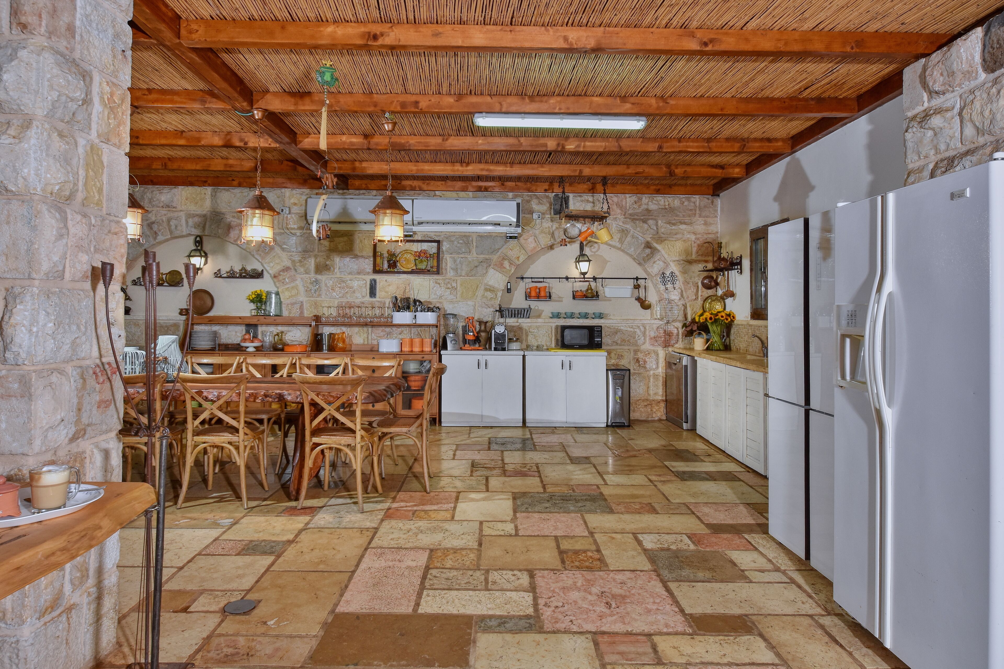 A rustic kitchen with stone walls, wooden beams, and a tiled floor.