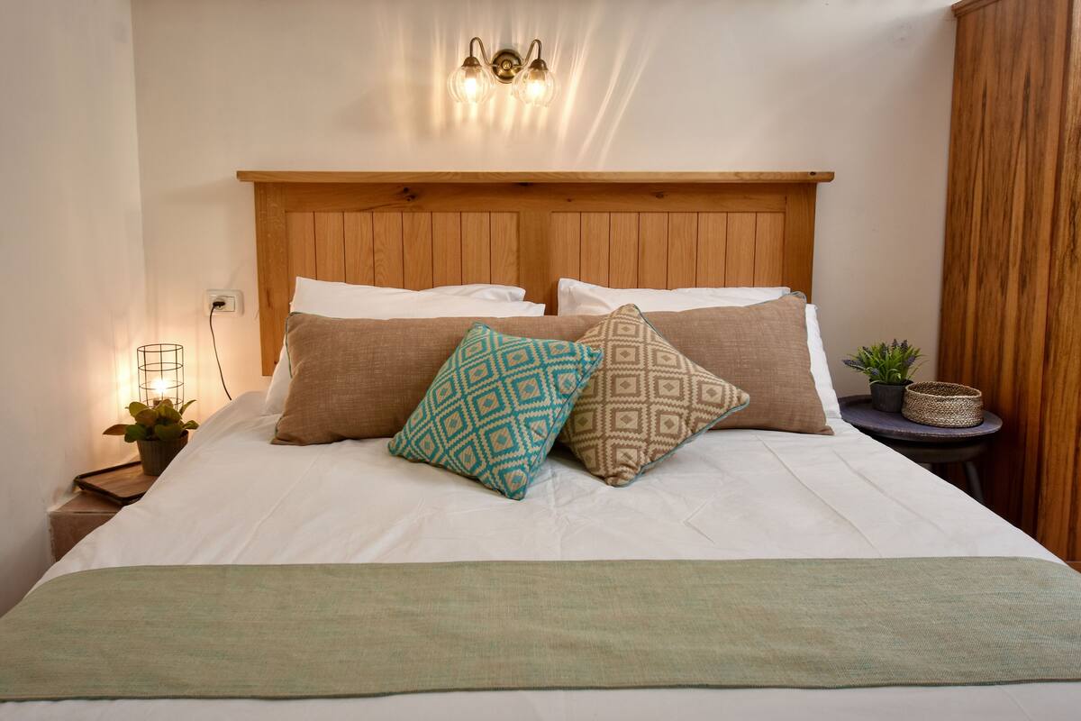 Uma cama bem arrumada com cabeceira de madeira, duas almofadas e um cobertor verde.