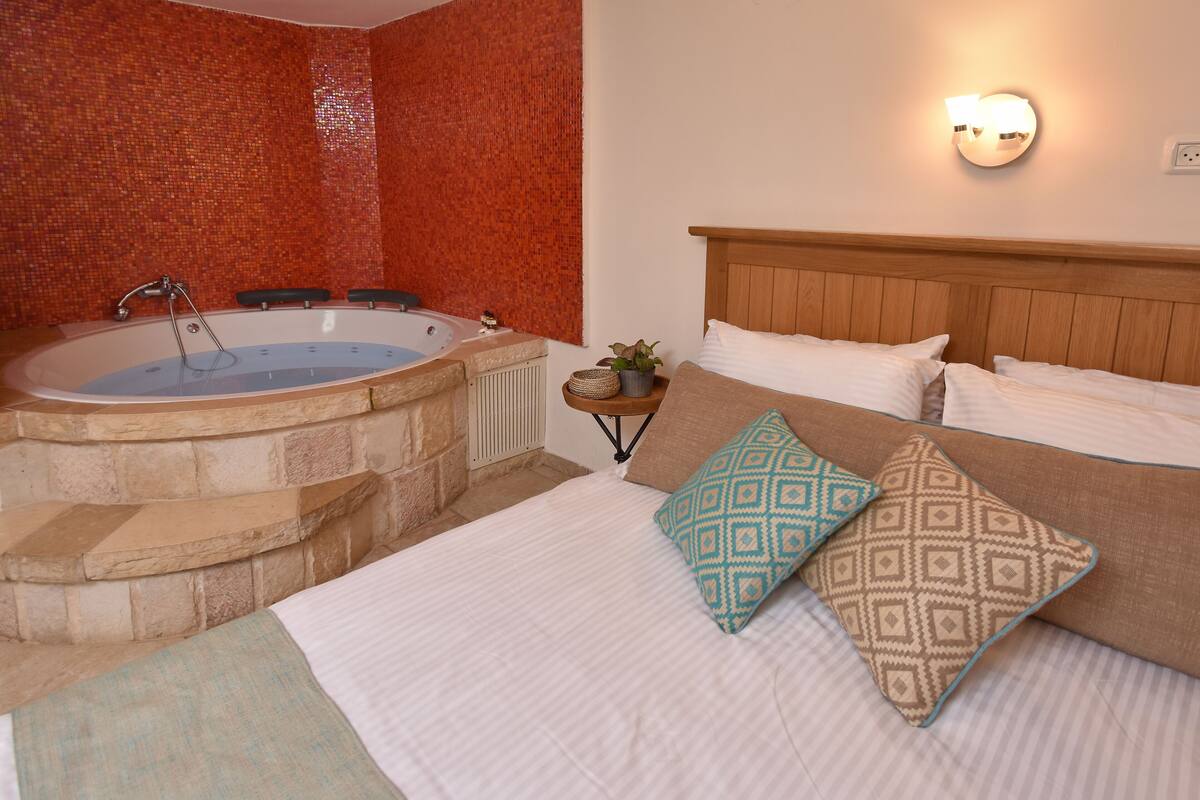 Quarto com cama grande, cabeceira de madeira e banheira integrada.