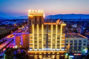 A multi-story hotel with illuminated signage, a prominent entrance, and a view of the surrounding urban area. - Huilong Hotel (Tiantai County)