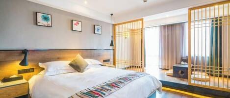 A modern hotel room with a large bed, bedside tables, a nightstand, a window with curtains, and a decorative screen.