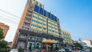 Un hotel su più piani con un ingresso evidente, diversi balconi e un'area di parcheggio con auto.