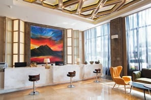 A reception area with a large painting, a reception desk, bar stools, and seating. - Huilong Hotel (Tiantai County)