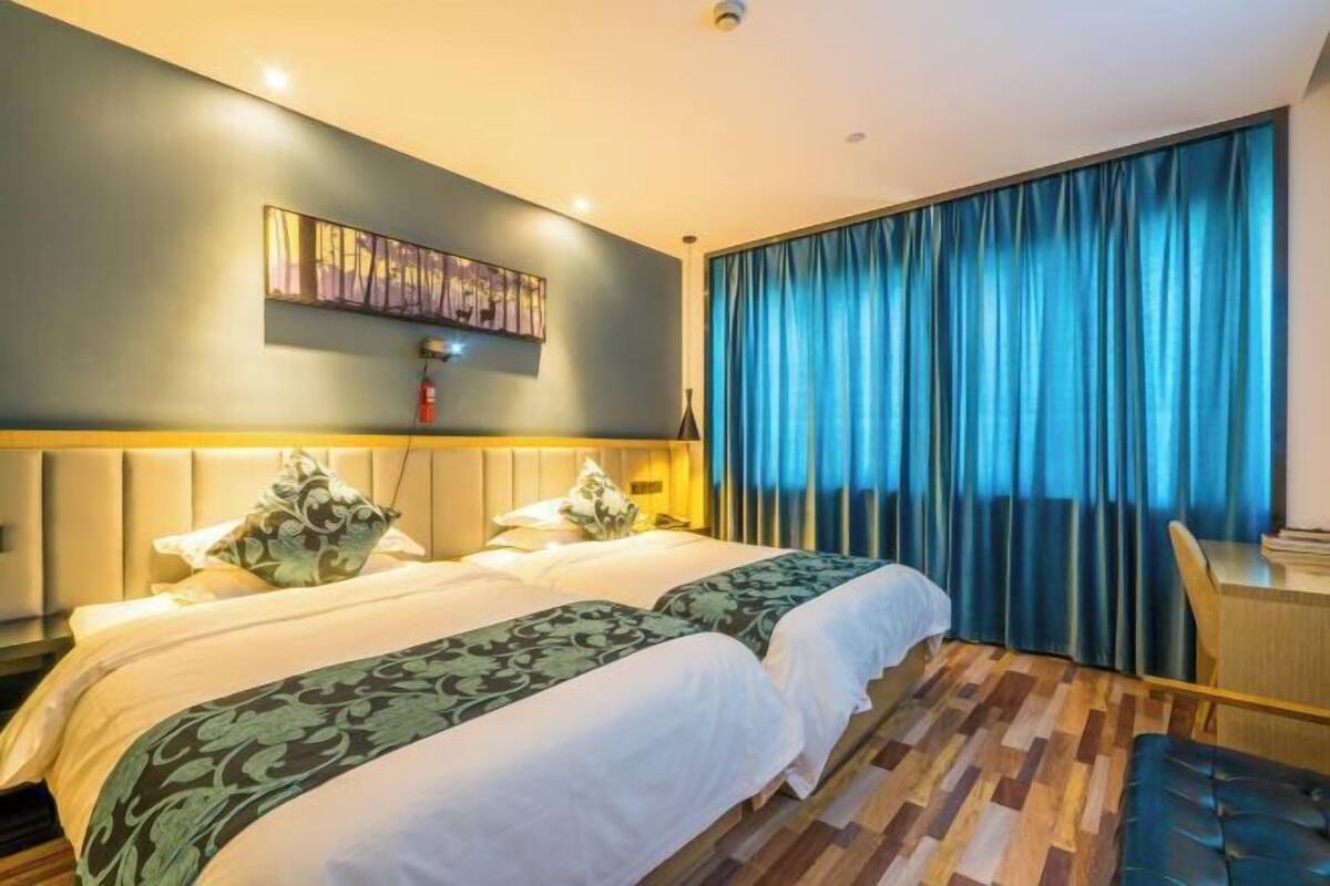 Une chambre d’hôtel avec deux lits, un bureau, une chaise, un tableau au mur et une fenêtre avec des rideaux.