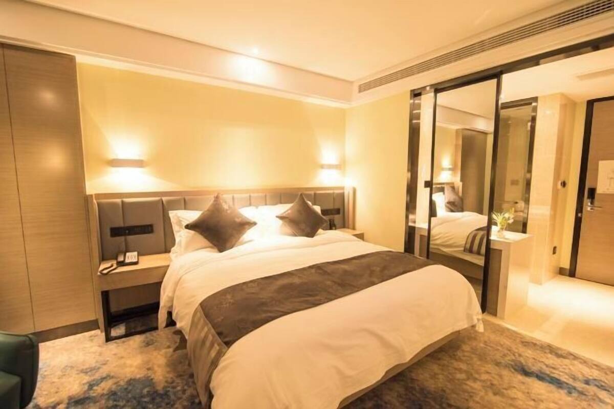 Une chambre d’hôtel avec un grand lit, des tables de chevet, un miroir et une porte coulissante donnant accès à la salle de bain.