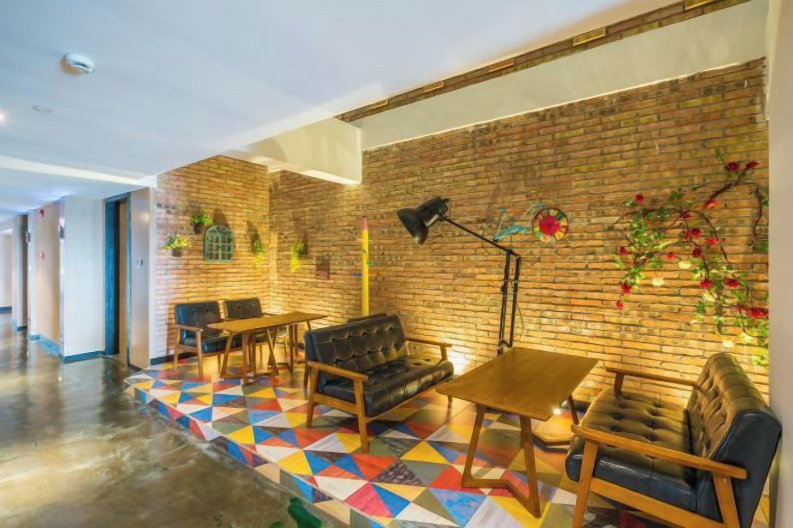 Un hall d’hôtel avec un mur en briques, un sol aux motifs géométriques colorés et divers espaces aménagés avec des canapés et des tables.