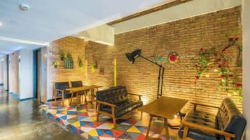 Un hall d’hôtel avec un mur en briques, un sol aux motifs géométriques colorés et divers espaces aménagés avec des canapés et des tables.