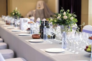 Una mesa de banquete dispuesta con cristalería transparente, platos y centros de mesa florales.