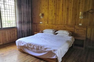 Quarto com painéis de madeira, uma cama, duas mesas de cabeceira e uma janela com cortinas.