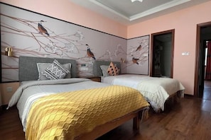 A bedroom with two beds, a large mural of birds on the wall, and a wooden floor.
