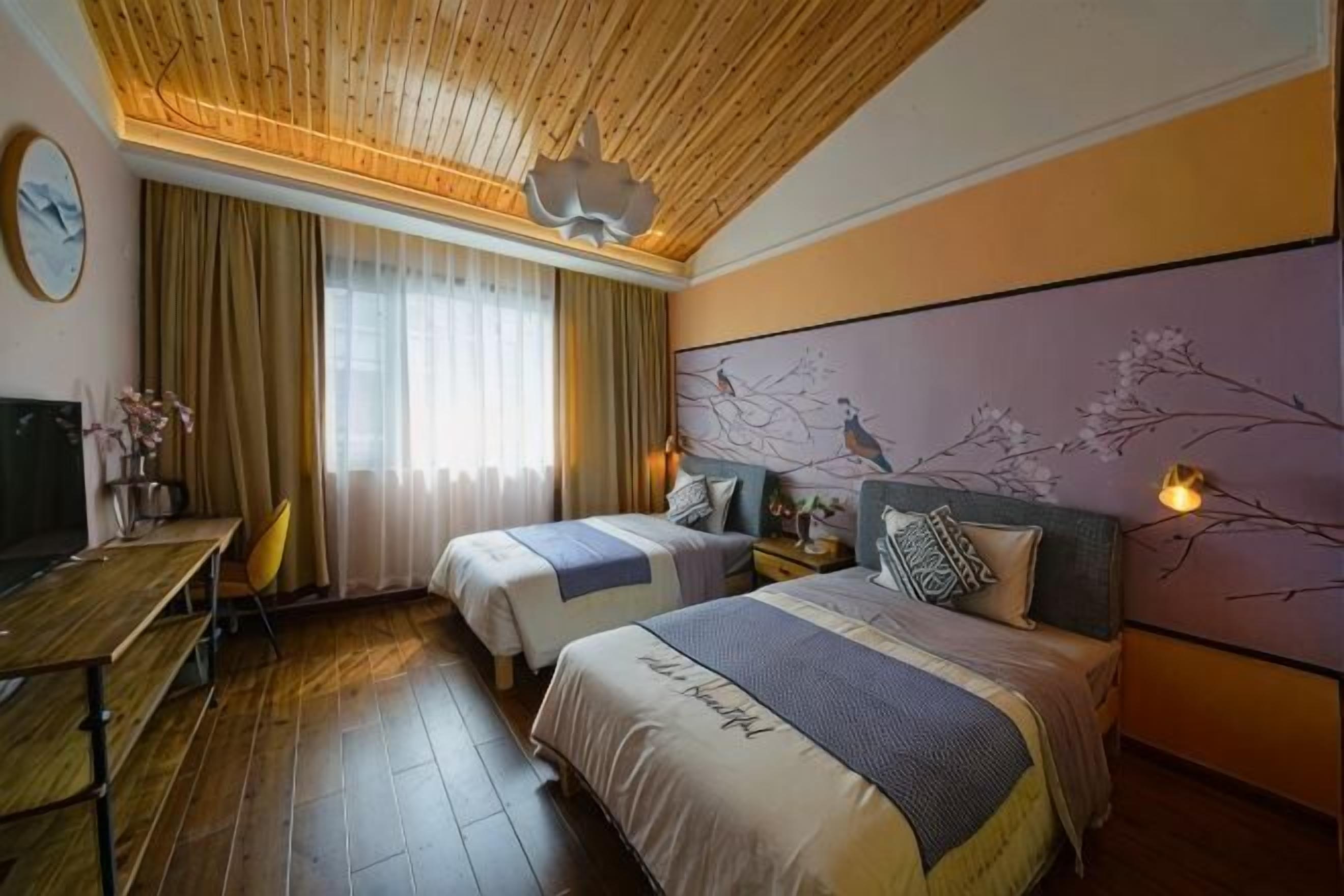 Ein Hotelzimmer mit zwei Betten, einem Schreibtisch, einem Fernseher und einem großen Fenster mit Vorhängen.