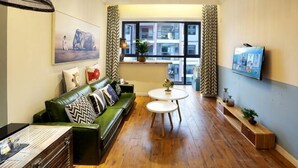 A furnished living room with a sofa, a coffee table, a TV, and a window with curtains. - Black Valley Purple Rose Inn (Chongqing)
