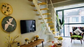 A modern living room with a wooden staircase, a flat-screen TV, a wooden coffee table, and a colorful armchair. - Black Valley Purple Rose Inn (Chongqing)