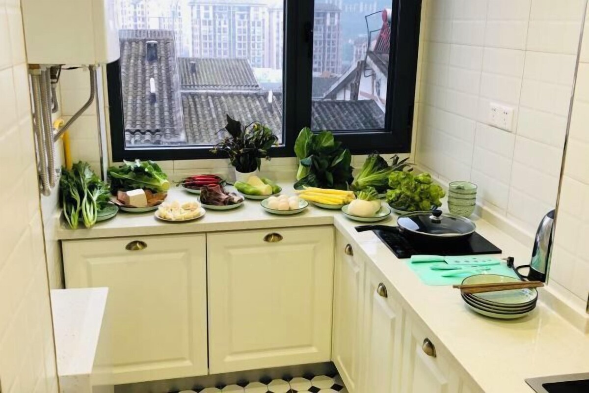 A kitchen with a window view, a sink, and various vegetables on the counter.