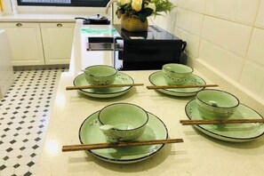 A kitchen with a tiled floor, a countertop with green dishes and chopsticks, and a vase with flowers on the counter. - Black Valley Purple Rose Inn (Chongqing)