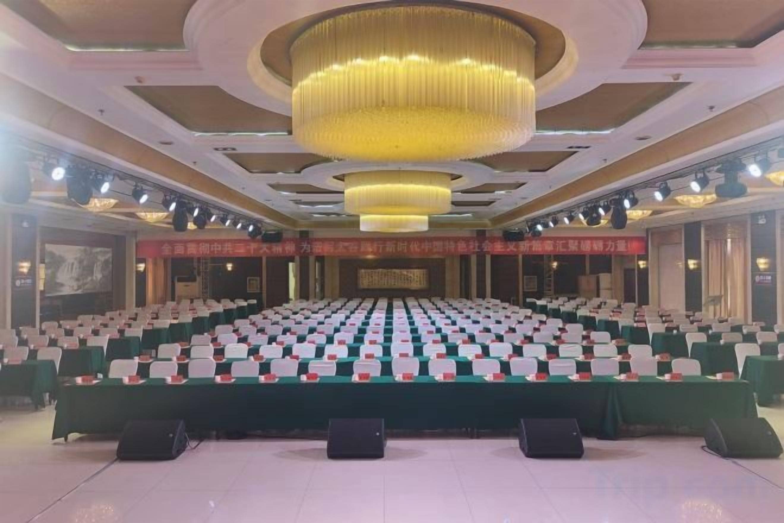 Un salón de conferencias con filas de mesas, una gran lámpara de araña y un escenario.