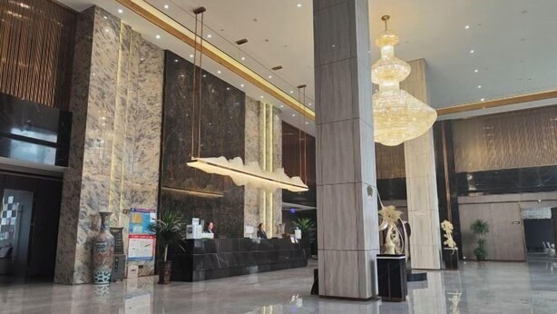 Un vestíbulo de hotel moderno con paredes de mármol, una recepción y una gran lámpara de araña.