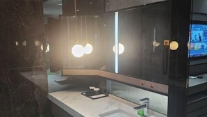 Un baño moderno con un espejo grande, dos lavamanos y una pantalla de televisión.
