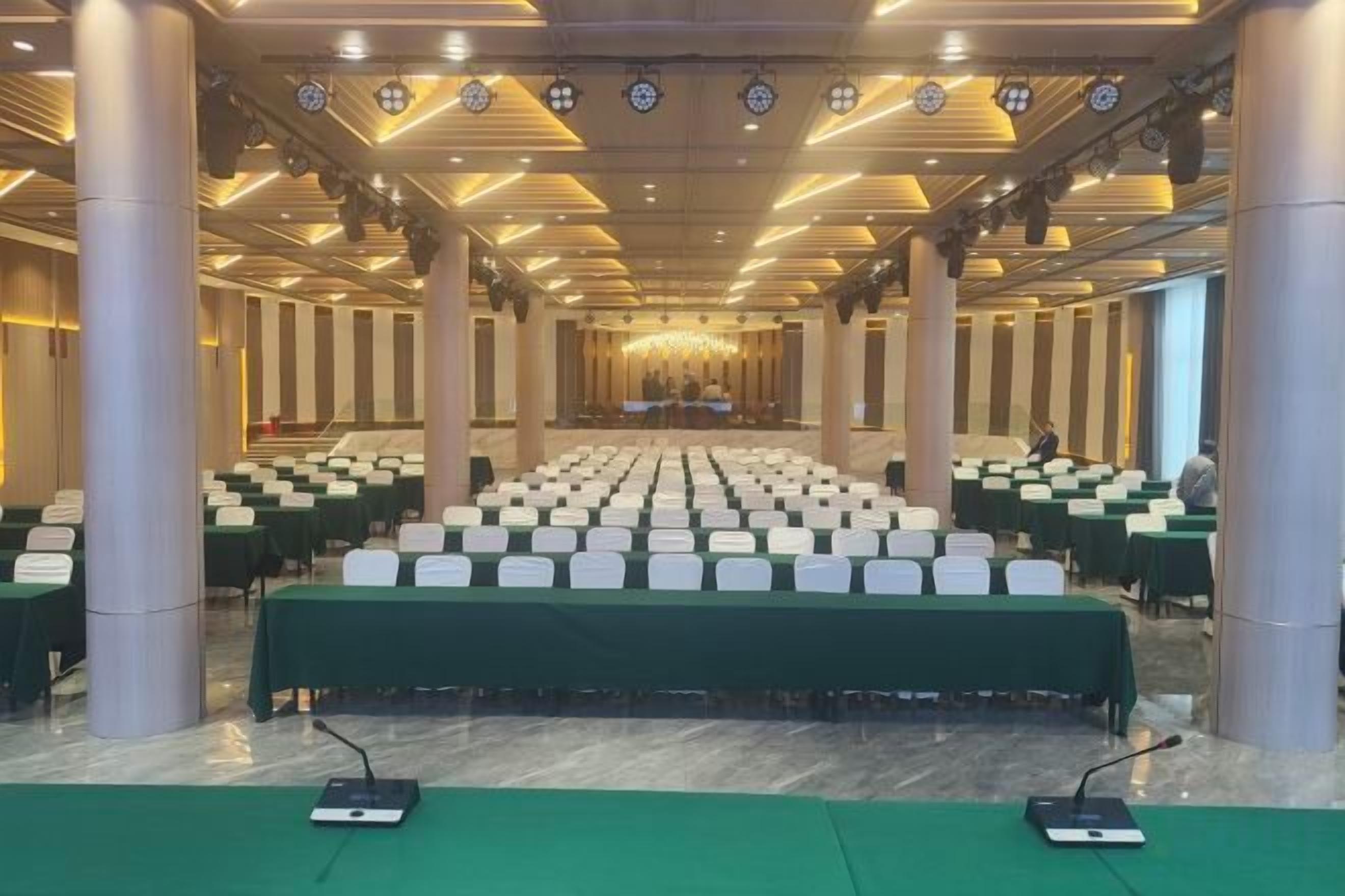 A conference room with rows of tables and chairs, a stage at the front, and a chandelier.