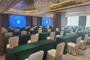 Un salón de conferencias con filas de mesas y sillas, pantallas grandes y un candelabro.