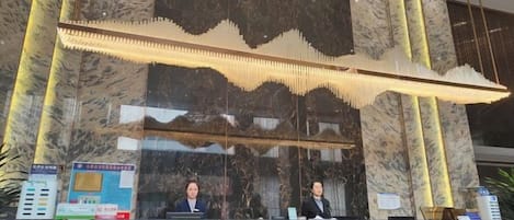 A reception desk with a marble wall and a large chandelier.