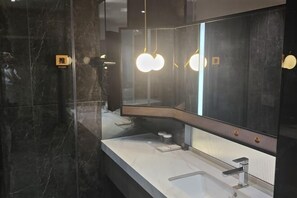 A modern bathroom with a large mirror, marble walls, and a white countertop. - Yiyuan Hotel (Jinzhong)