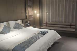 A neatly made bed with a white and gray striped bedspread, a bedside table with a lamp, and a window with curtains. - Yiyuan Hotel (Jinzhong)