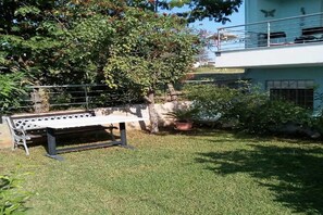A grassy outdoor area with a metal bench, potted plants, and a building with a balcony. - Cheerful holiday home in Preveza  with garden (Preveza)