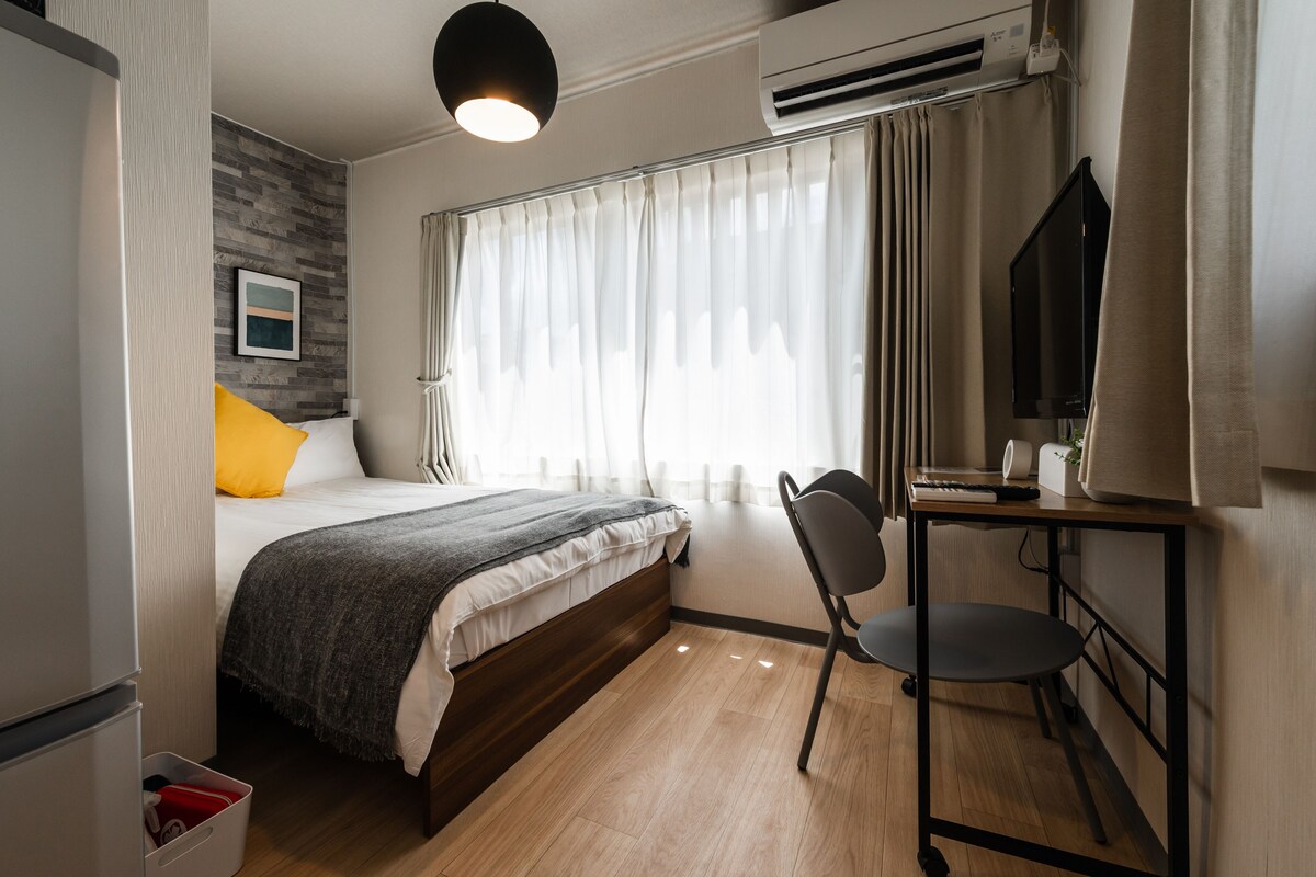 Una habitación de hotel moderna con una cama de madera, un escritorio con una silla, un televisor y un equipo de aire acondicionado.