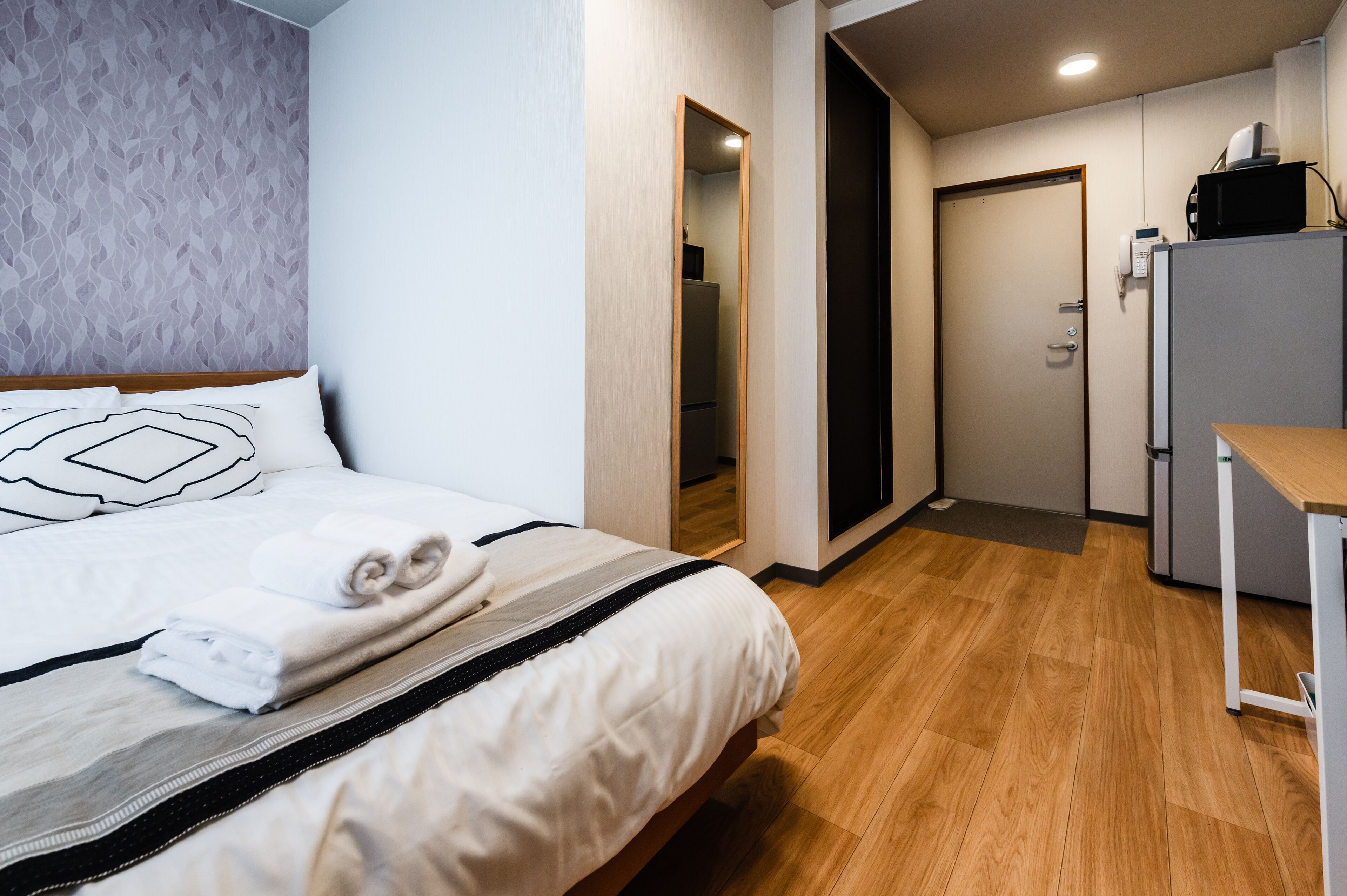 Habitación de hotel con cama, escritorio, microondas y puerta que da a un baño.