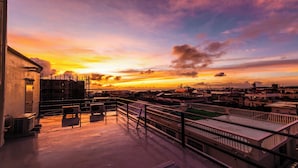 Une terrasse sur le toit offrant une vue sur la ville au coucher du soleil, avec une rambarde et des unités de climatisation.