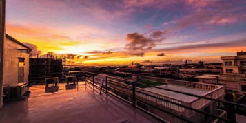 Une terrasse sur le toit offrant une vue sur la ville au coucher du soleil, avec une rambarde et des unités de climatisation.