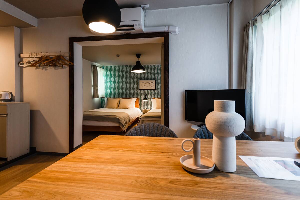 Camera d'albergo con tavolo in legno, un vaso, una tazza e un letto con una parete a motivi verdi.