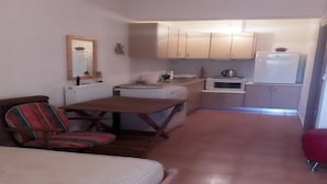 A compact kitchen with basic appliances, a dining area with a table and chairs, and a small mirror on the wall. - Holiday Home in Greece near the Beach (Preveza)