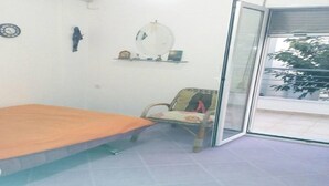 A room with a bed, a chair, a shelf with decorative items, a clock, and a window with a view of the outside. - Holiday Home in Greece near the Beach (Preveza)