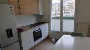 A compact kitchen with a refrigerator, oven, and sink. There is a window providing a view of buildings outside. - 3 rooms Grenoble - Saint Martin d'heres (Saint-Martin-d'Hères)