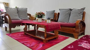 A living room with a wooden sofa, striped pillows, a red table, and a floral rug. - OYO Homes 90567 Barakah Homestay (Tawau)